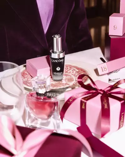 Productos de belleza Lancome y cajas de regalo rosadas dispuestas sobre una mesa de comedor festiva.
