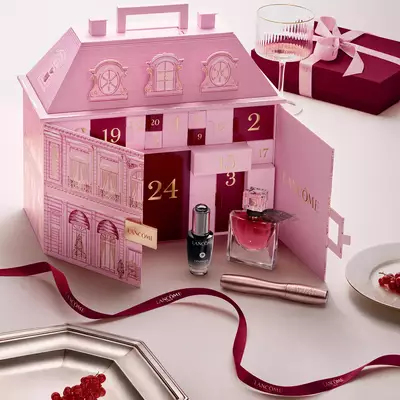 Un calendario de adviento Lancome rosado con forma de casona, abierto y exhibido junto a productos de belleza y una cinta roja.