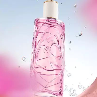 Un frasco de perfume rosado claro con un diseno de vidrio texturizado, sobre un fondo de cielo azul claro, con gotas de agua salpicando a su alrededor. El frasco se ve a traves de una abertura circular en una pared rosada texturizada, y hay flores rosadas difuminadas en primer plano y en el fondo.