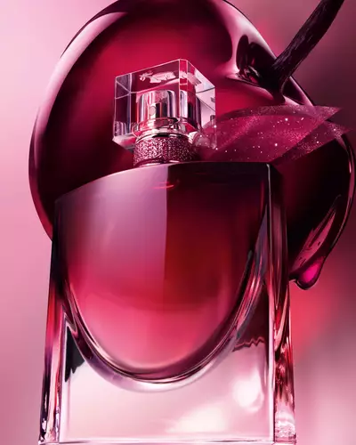 A close-up artistic shot of the burgundy perfume bottle positioned in front of a large, glossy dark cherry.