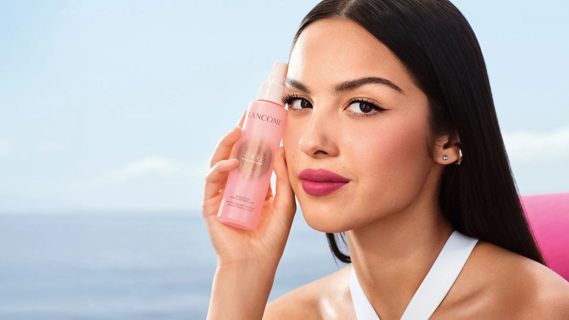 Modelo sosteniendo el spray Lancôme Skin Idole Magnet junto al mar.